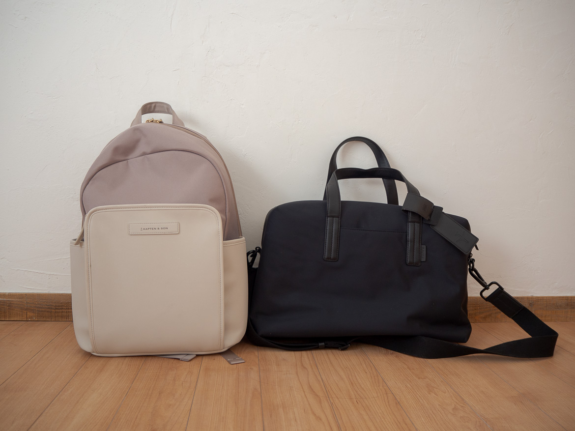 Ein Rucksack in beige steht neben einer schwarzen Reisetasche
